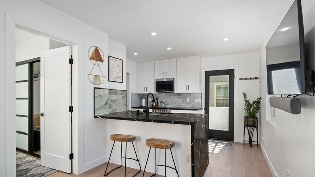 A modern kitchen with white cabinets, a black countertop, and two wooden stools. - Modern Retreat Steps to the Beach! (San Diego)