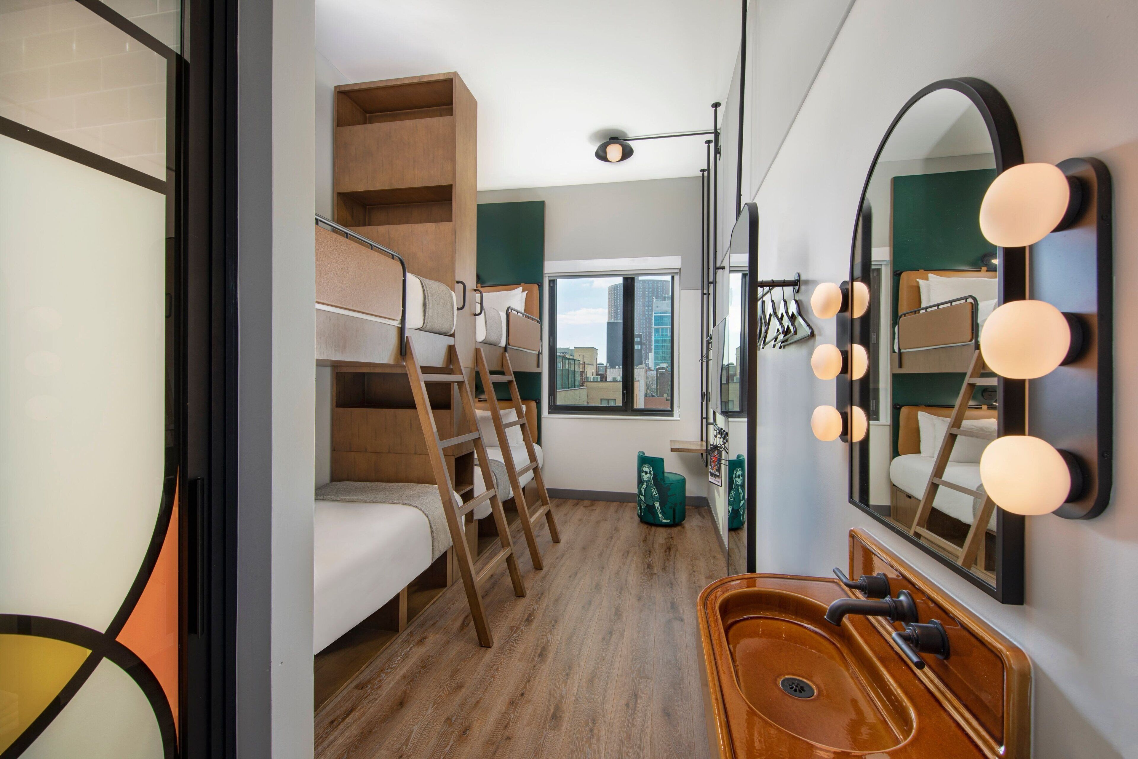 Una habitación de hotel compacta con una cama litera, un tocador de madera con lavabo y un espejo grande con iluminación.