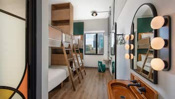 Una habitación de hotel compacta con una cama litera, un tocador de madera con lavabo y un espejo grande con iluminación.