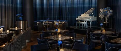 Uma área de jantar luxuosa com um piano de cauda, cortinas azul-escuro e arranjos de assentos elegantes.