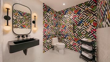 Casa de banho com lavatório preto, sanita e espelho com iluminação embutida na parede.