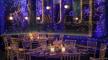 A restaurant with round tables set for dining, illuminated by ambient lighting and decorative wall art.