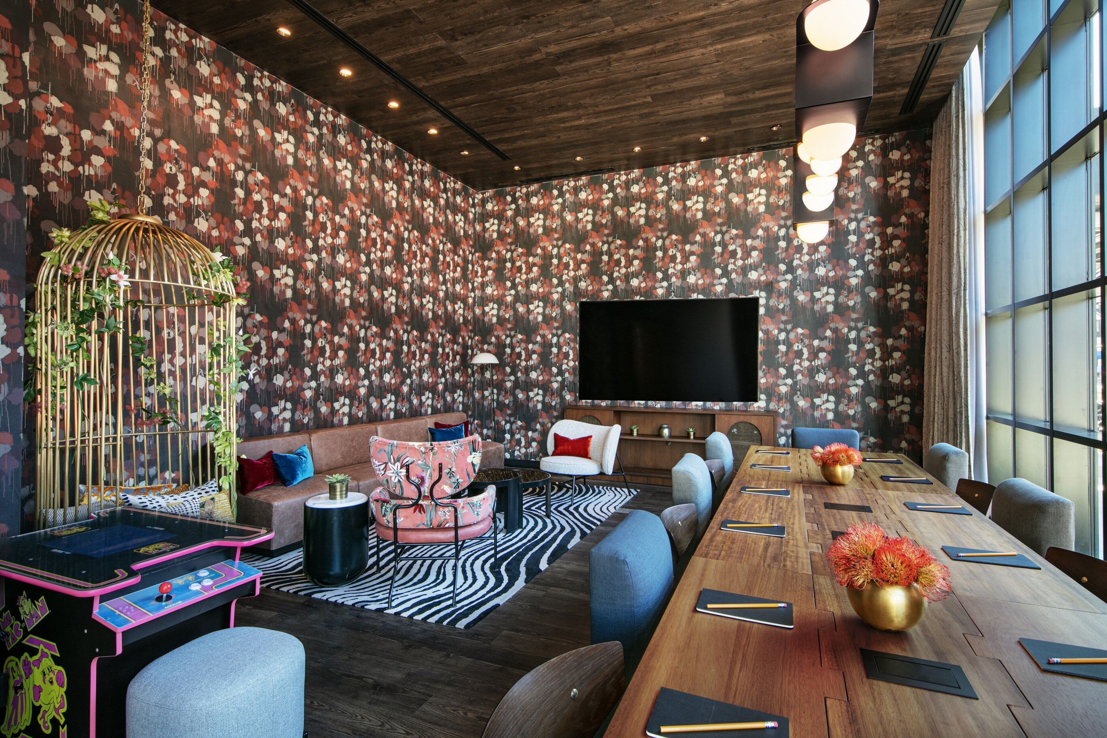 A modern conference room with a long wooden table, comfortable seating, a large flat-screen TV, and a decorative birdcage with plants.