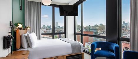 A modern hotel room with a large bed, a desk, a laptop, and a TV.