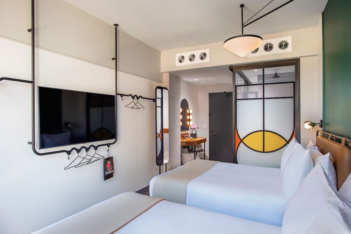 Ein Hotelzimmer mit Bett, Fernseher, Spiegel und Schminktisch mit Beleuchtung.