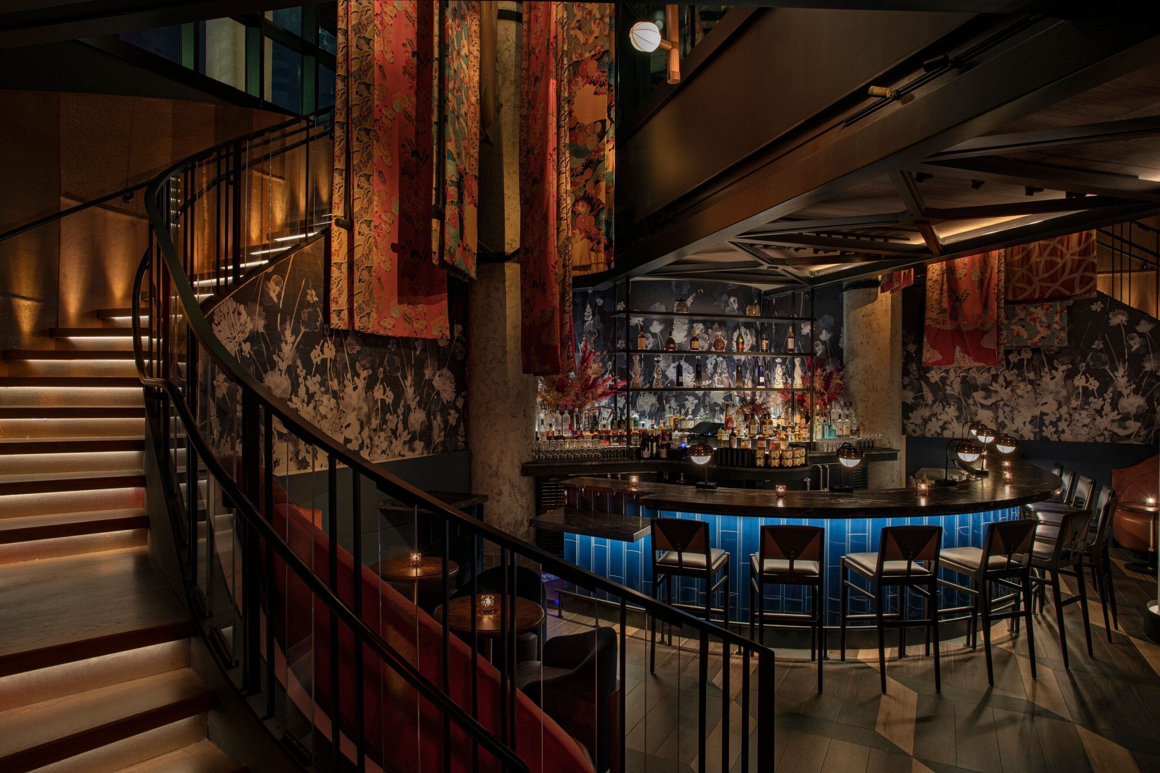Eine Bar mit einer gebogenen Theke, Barhocker und einer Treppe mit Geländer.