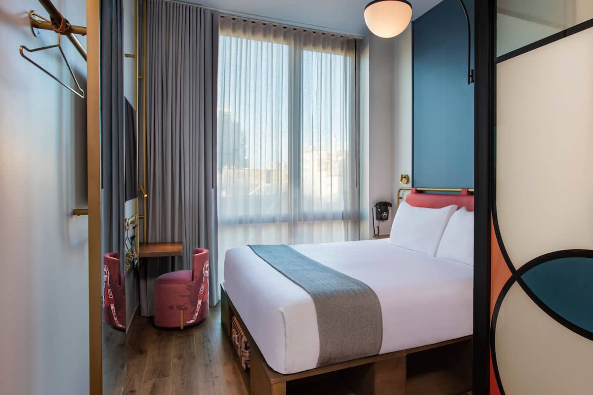Ein Hotelzimmer mit Bett, Schreibtisch, Stuhl und einem fenster mit Vorhängen.