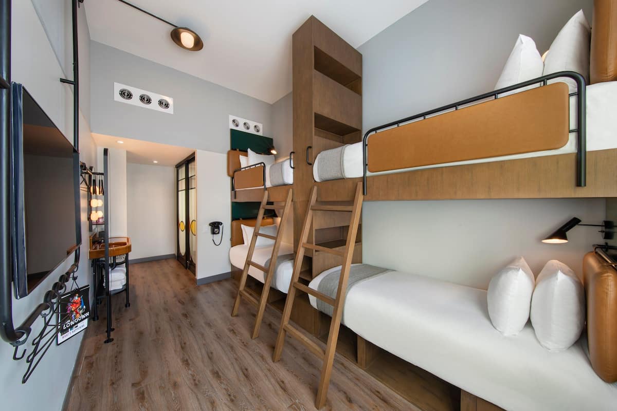 Ein kompaktes Hotelzimmer mit Stockbetten, einer Schlafcouch, einem Fernseher und einer kleinen Küchenzeile.
