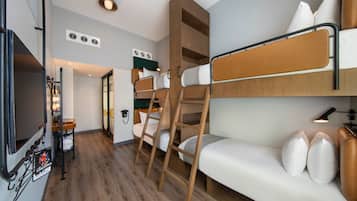 Habitación de hotel compacta con literas, sofá, televisión y una pequeña kitchenette.