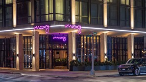A hotel entrance with a neon sign, large windows, and a parked car. - Moxy NYC Lower East Side (New York)