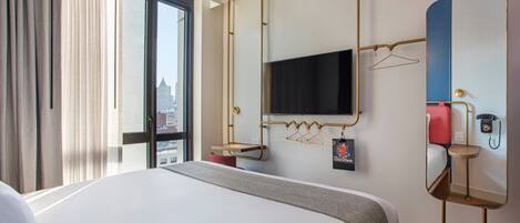 Une chambre d’hôtel avec un grand lit, un téléviseur fixé au mur, un miroir et une fenêtre avec des rideaux.
