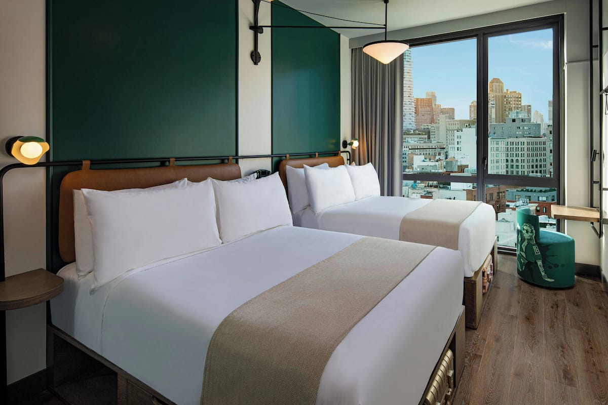 Ein Hotelzimmer mit zwei Betten, Blick auf die Stadt und einer grünen Akzentwand.