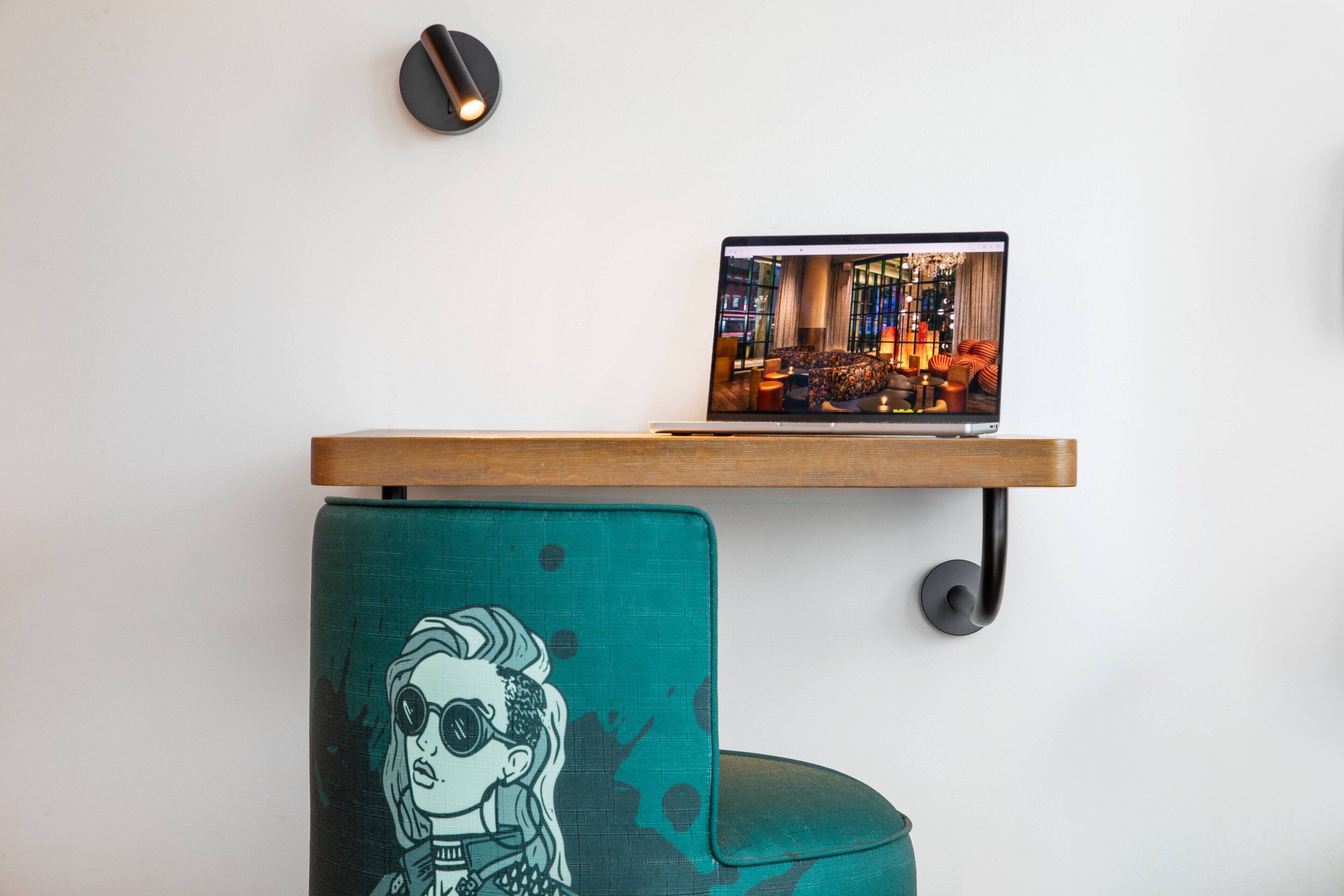 A laptop on a wooden shelf above a teal chair with a graphic design.