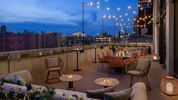 Terraza en la azotea con mobiliario exterior, luces colgantes y vistas a la ciudad.