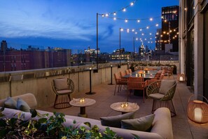 A rooftop terrace with outdoor seating, string lights, and a city skyline view. - Moxy NYC Lower East Side (New York)