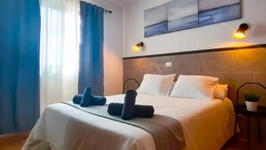Een hotelkamer met een bed, een hoofdbord, een aan de muur hangend schilderij en een kleintje tafeltje met een plant.
