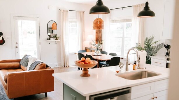 Une cuisine moderne avec un îlot central, un coin repas avec une table et des chaises, et un salon avec un canapé.