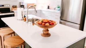 Une cuisine avec un plan de travail blanc, un saladier en bois rempli de pommes, un évier et un réfrigérateur en acier inoxydable.