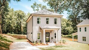 Une maison à deux étages avec un porche à l’avant, une allée et une pelouse bien entretenue.