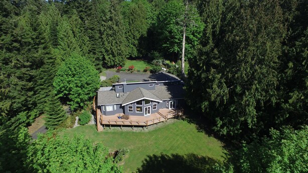 A two-story house with a deck, surrounded by dense forest. - Modern studio with hot tub and patio access  (Poulsbo)