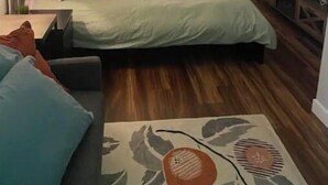 A bedroom with a bed, a nightstand, a lamp, a wall-mounted TV, and a small table with a decorative item. - Modern studio with hot tub and patio access  (Poulsbo)