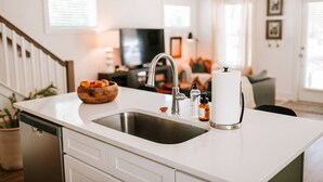 Una cocina moderna con encimera blanca, pileta de acero inoxidable y un bol de madera con fruta.