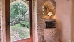 A stone-built room with a door leading to a garden, a stone fireplace with a lamp, and a tiled floor. - Ti Kaouenn - PLOUARET (PLOUARET)