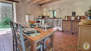 A rustic kitchen with a dining table set for four, a stone wall, and a view of the garden. - Ti Kaouenn - PLOUARET (PLOUARET)