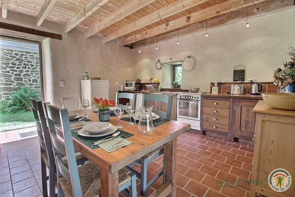 A rustic kitchen with a dining table set for four, a stone wall, and a view of the garden.