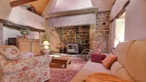 A cozy living room with a stone fireplace, floral sofa, and a wooden table.