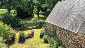 A stone building with a sloped roof, surrounded by a well-maintained garden with various plants and a small pond. - Ti Kaouenn - PLOUARET (PLOUARET)