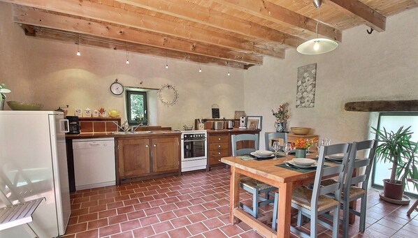 A rustic kitchen with wooden cabinets, a brick floor, and a dining area with a wooden table and chairs.
