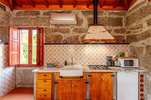 Cocina rústica con paredes de piedra, armarios de madera, un lavamanos blanco, microondas y estufa a gas.