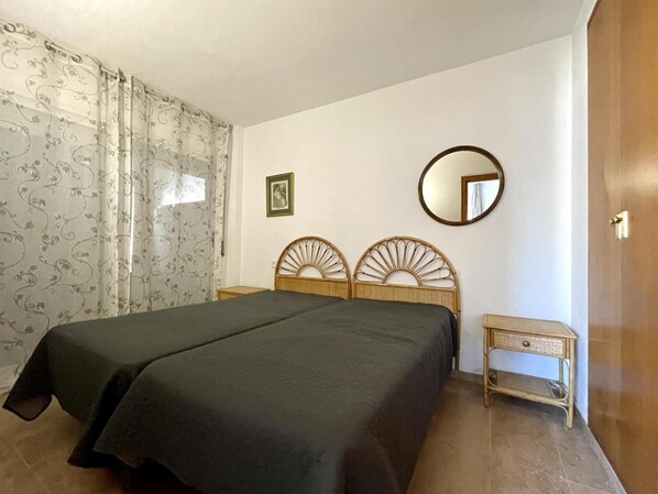 A bedroom with a bed, a bedside table, a mirror, and a picture on the wall.