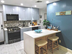 A modern kitchen with a central island, bar stools, a microwave, and a blue accent wall.