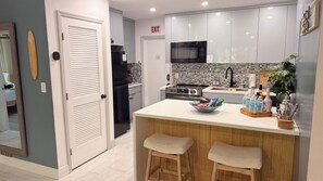 A modern kitchen with a central island, wooden stools, and a microwave above the sink. - Salt and Sage Stay I Designer 4BR/2 Bath Retreat I Plunge Pool I 10 min to Beach (hollywood)