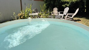 Ein Schwimmbecken mit klarem Wasser, umgeben von weißen Stühlen und Topfpflanzen.