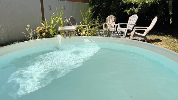 Una piscina con agua cristalina, rodeada de sillas blancas y plantas en macetas.