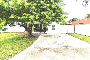 A residential area with a tree-lined driveway leading to a house with a white exterior and a small porch. - Salt and Sage Stay I Designer 4BR/2 Bath Retreat I Plunge Pool I 10 min to Beach (hollywood)