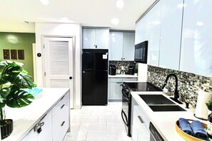 Eine moderne Küche mit weißen Schränken, einem schwarzen Kühlschrank, einer Mikrowelle und einer Kaffeemaschine.