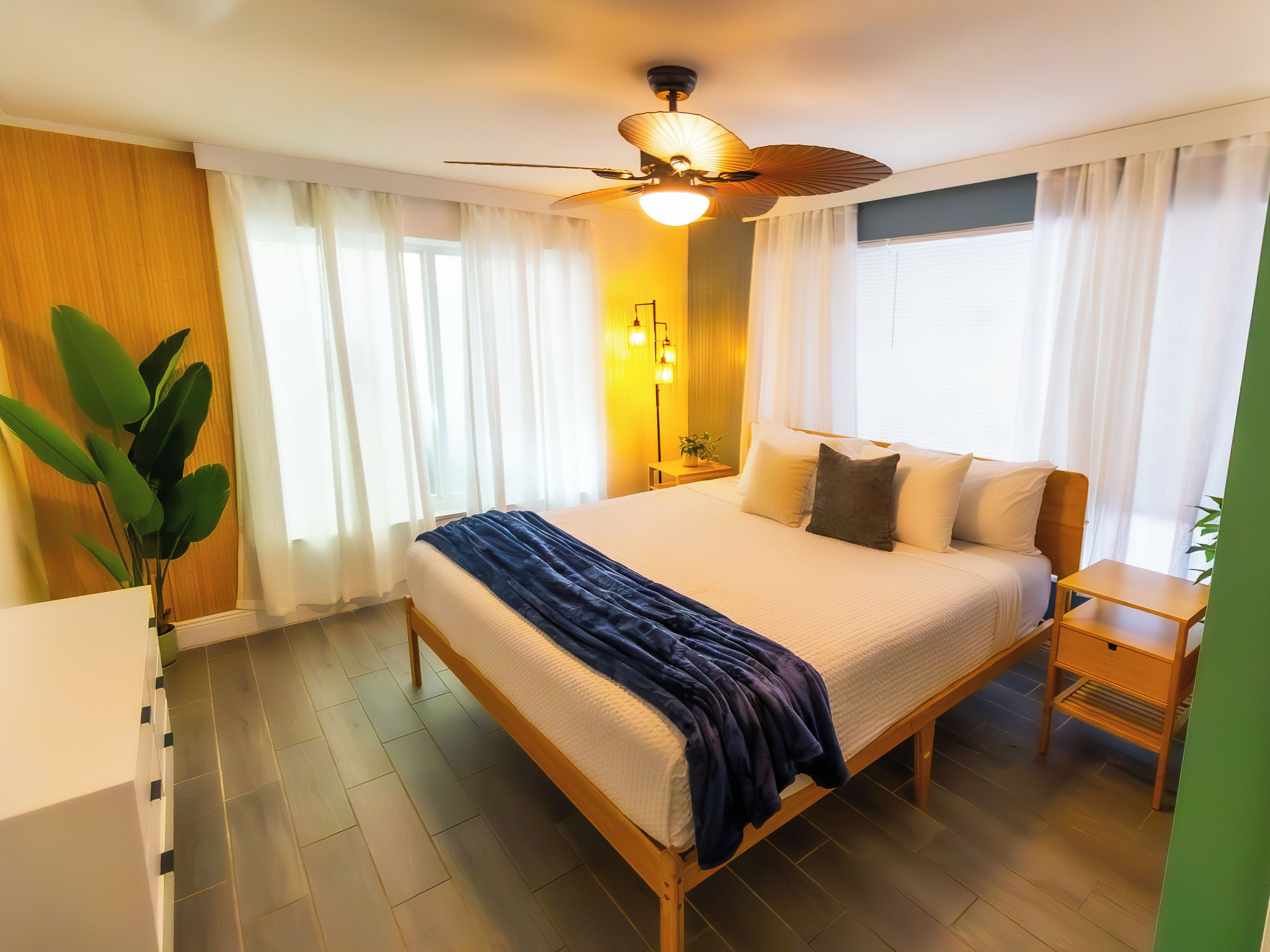 A hotel room with a bed, bedside tables, a ceiling fan, and a potted plant.