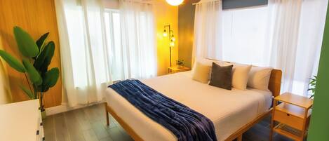 A hotel room with a bed, bedside tables, a ceiling fan, and a potted plant.