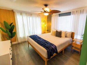 A hotel room with a bed, bedside tables, a ceiling fan, and a potted plant.