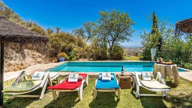 A poolside area with lounge chairs and a table with a bottle and glass. - Cortijo La Alberquilla Íllora by Ruralidays (Granada)
