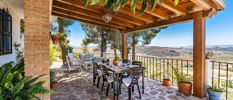 A covered outdoor patio with stone flooring, a wooden pergola, and a table with chairs.