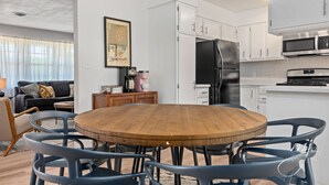A modern kitchen with white cabinets, a black refrigerator, and a wooden dining table with blue chairs.