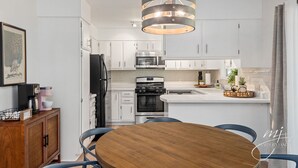 A modern kitchen with white cabinets, a central island, stainless steel appliances, and a wooden dining table.