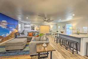 Relax in this stylish living space with a high ceiling, ceiling fan, and vibrant mural, featuring a comfortable sofa, coffee table, and bar stools.