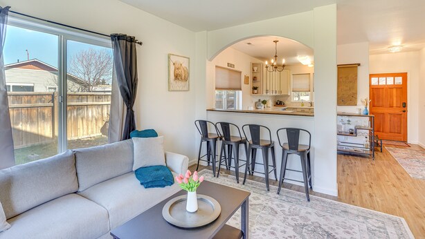 A living room with a sofa, a coffee table with a vase of flowers, and a view of the backyard through large windows. - Charming Bend Home w/ Porch & Yard: Great Location (Bend)