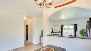 A spacious room with a dark wooden table, a decorative bowl, a chandelier, and a view of the outside through a window with curtains. - Charming Bend Home w/ Porch & Yard: Great Location (Bend)